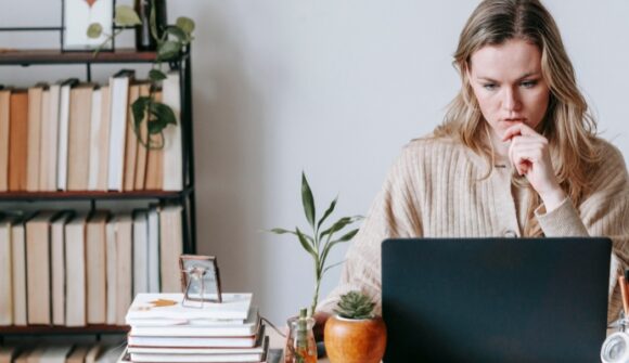 Nainen työskentelee keskittyneenä kannettavalla tietokoneella ja hakee yrityslainaa uudelle yritykselle rahoittaakseen liiketoiminnan käynnistämistä.