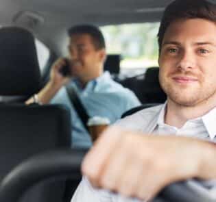 Mies ajaa autoa ja takapenkillä toinen matkustaja