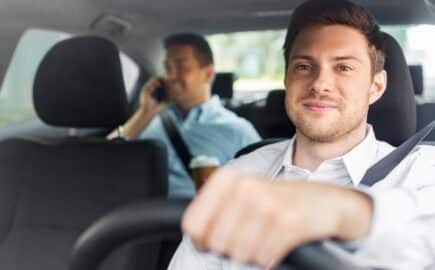 Mies ajaa autoa ja takapenkillä toinen matkustaja