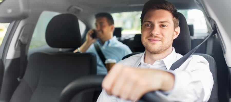 Mies ajaa autoa ja takapenkillä toinen matkustaja